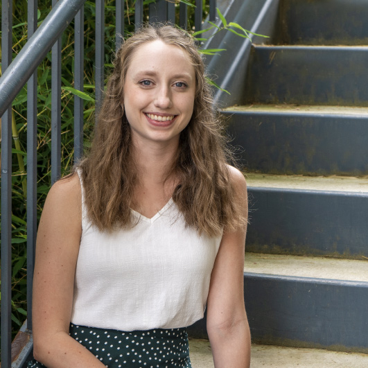 Abby Capps, social media specialist at Lead Dog Digital Tyler TX is sitting at the stairs in a white shirt.