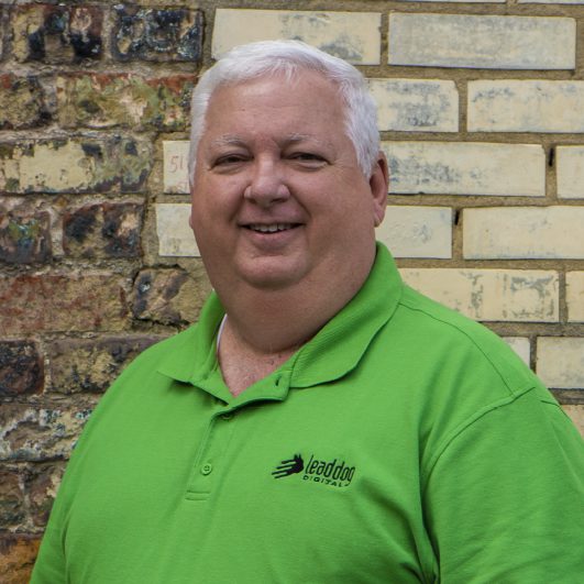 Joey Abna - digital strategist at Lead Dog Digital Tyler TX, sitting in front of the wall in a green shirt.