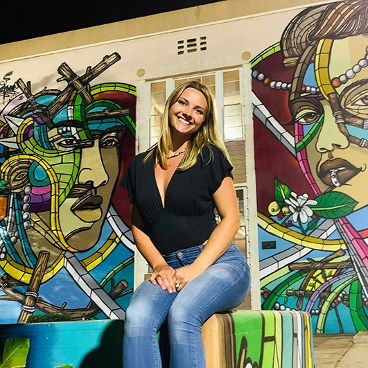 Elizabeth Freeman, graphic designer/account manager at Lead Dog Digital, sitting on a cozy bench in front of the vibrant mural.